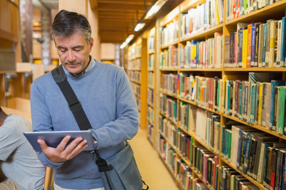 Man holding a tablet pc amongst shelves in a library